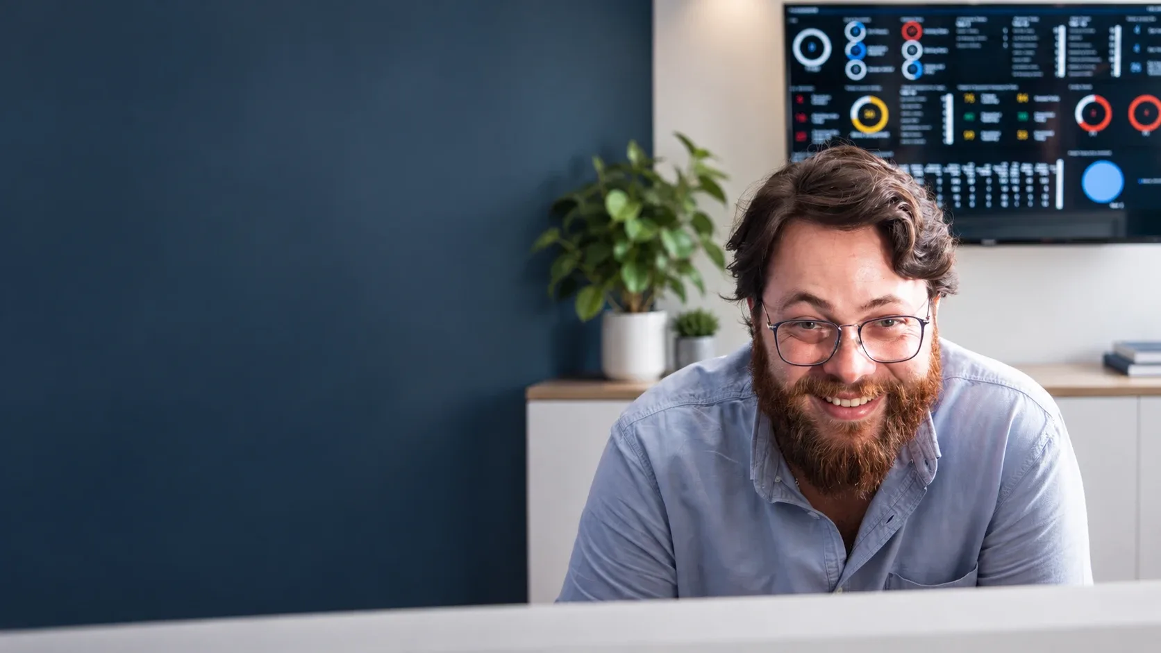 A smiling Solid Systems engineer at his desk, with the live service dashboard on the screen behind him