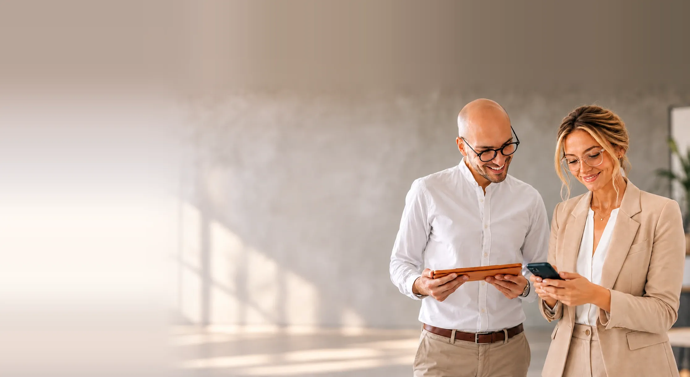 Two colleagues smiling as they work together on a tablet and a phone in a bright office