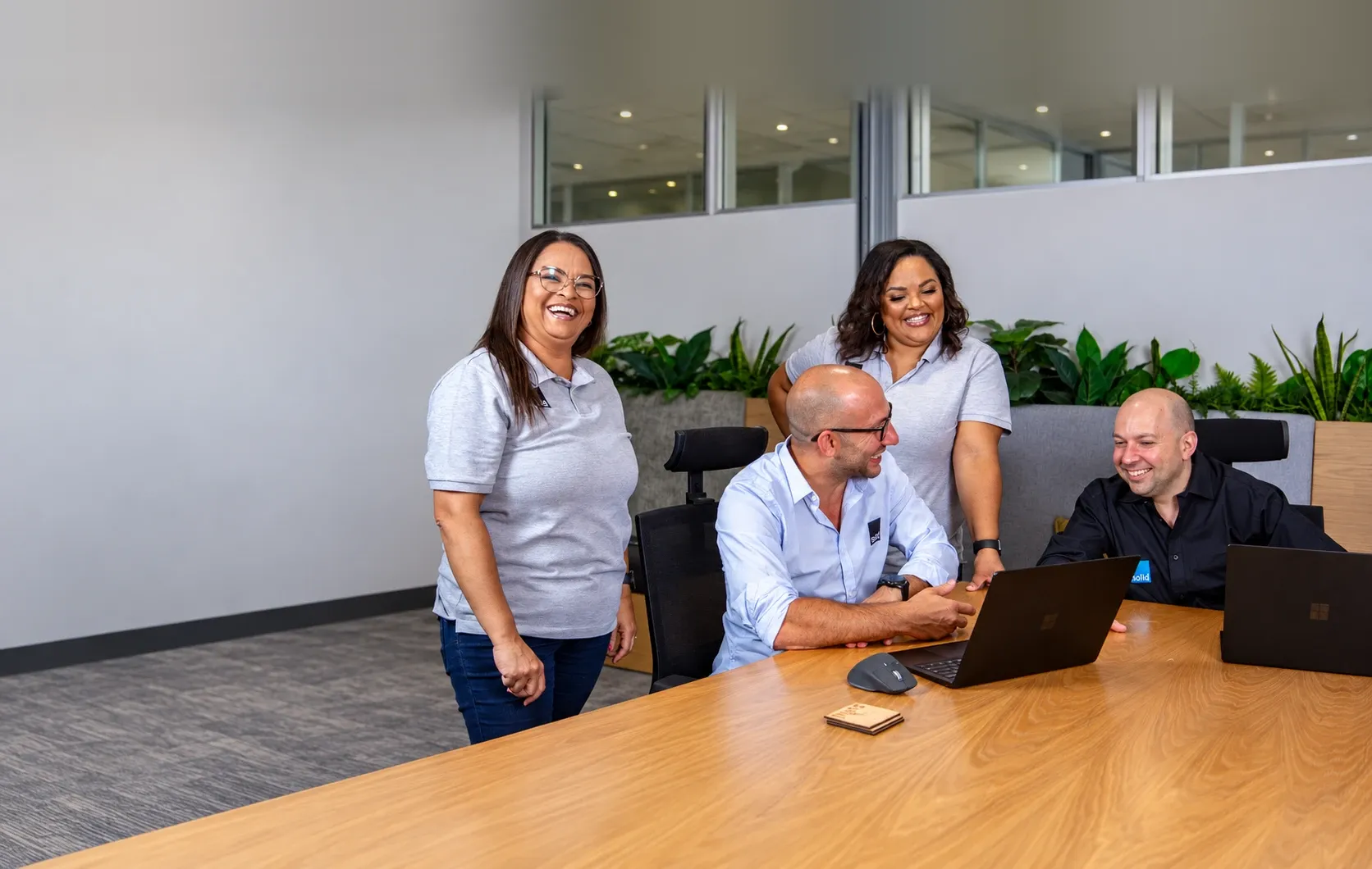 Four members of the Solid Systems team laughing together around a laptop in the office