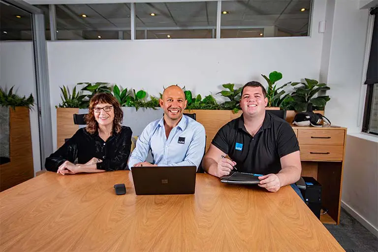 Three members of the Solid Systems team smiling around a meeting table