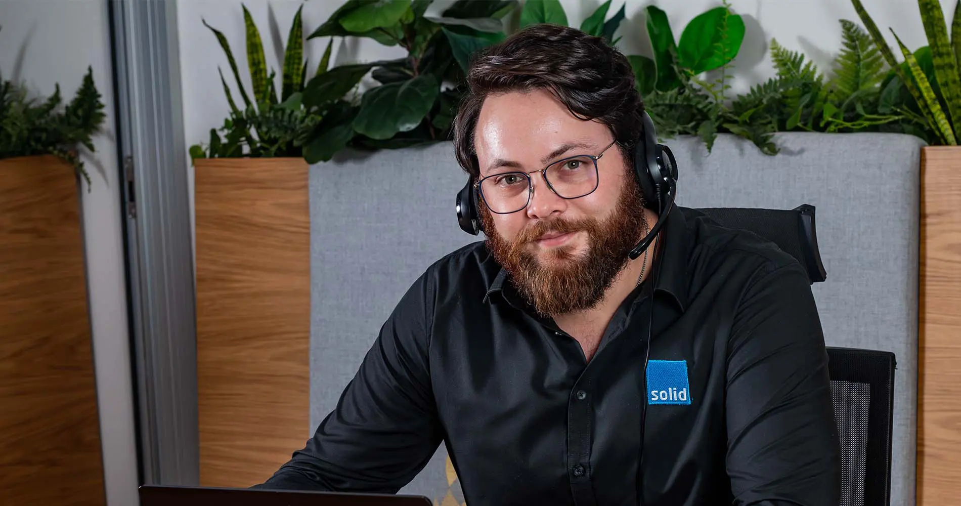 A Solid Systems IT Pro wearing a headset at the helpdesk, smiling at the camera