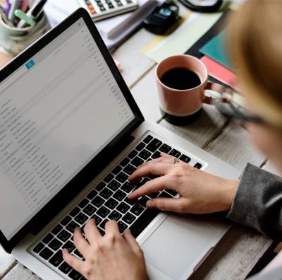 Hands typing on a laptop showing an email inbox, next to a cup of coffee