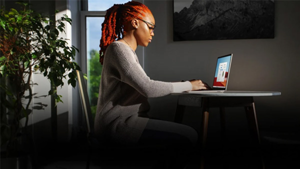 A woman working on a laptop at a desk by a window