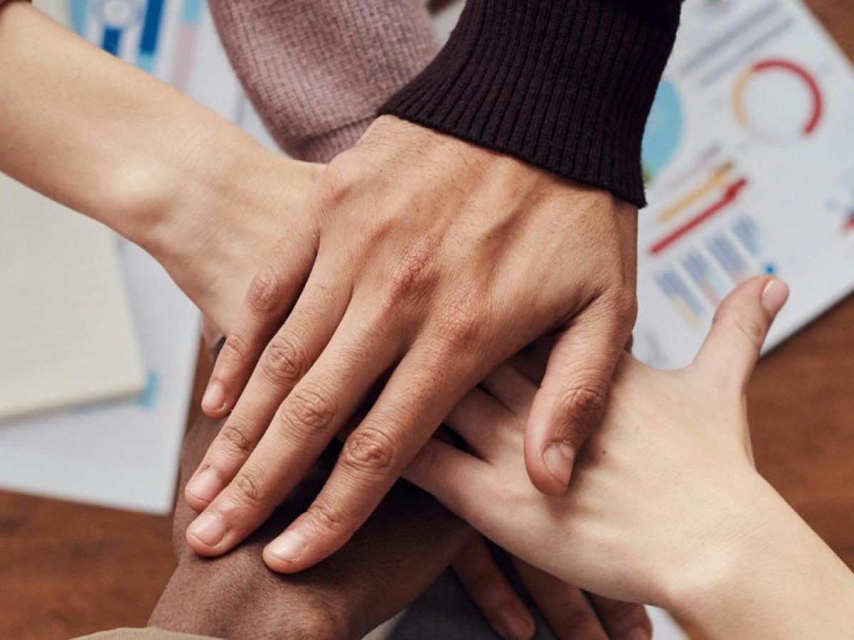 Colleagues stacking their hands together over a desk, a sign of partnership